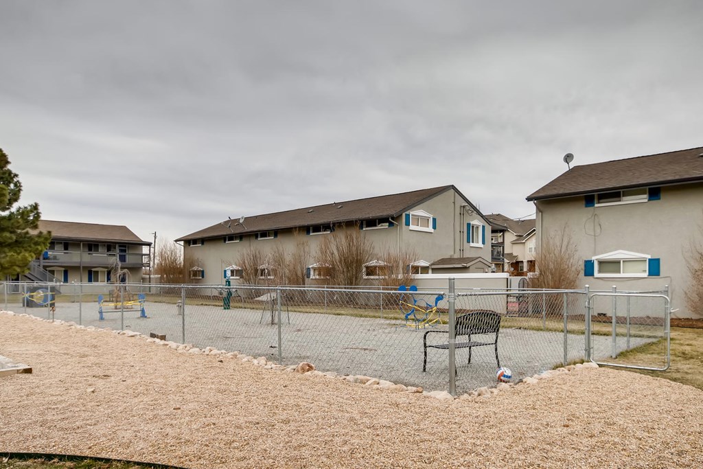 A playground with a bench and a fence in front of houses.