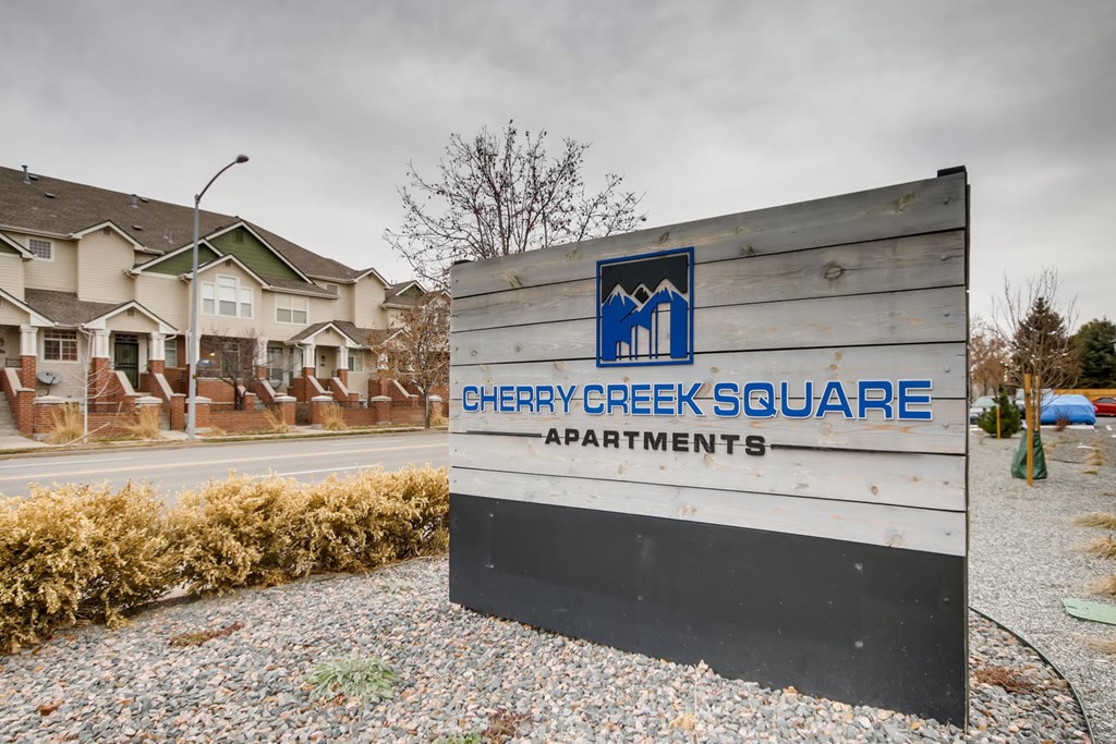 A sign for Cherry Creek Square Apartments in front of a building.