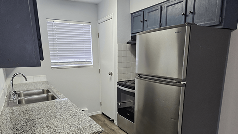 A kitchen with a stainless steel refrigerator and a sink with granite countertops.