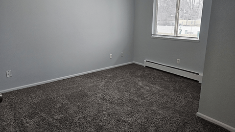 A room with a grey carpet and a window.