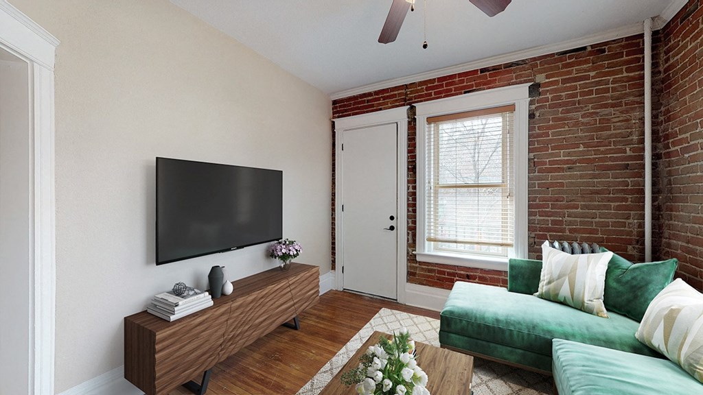 a living room with a green couch and a tv on a brick wall