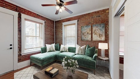 a brick walled living room with a green couch and a ceiling fan