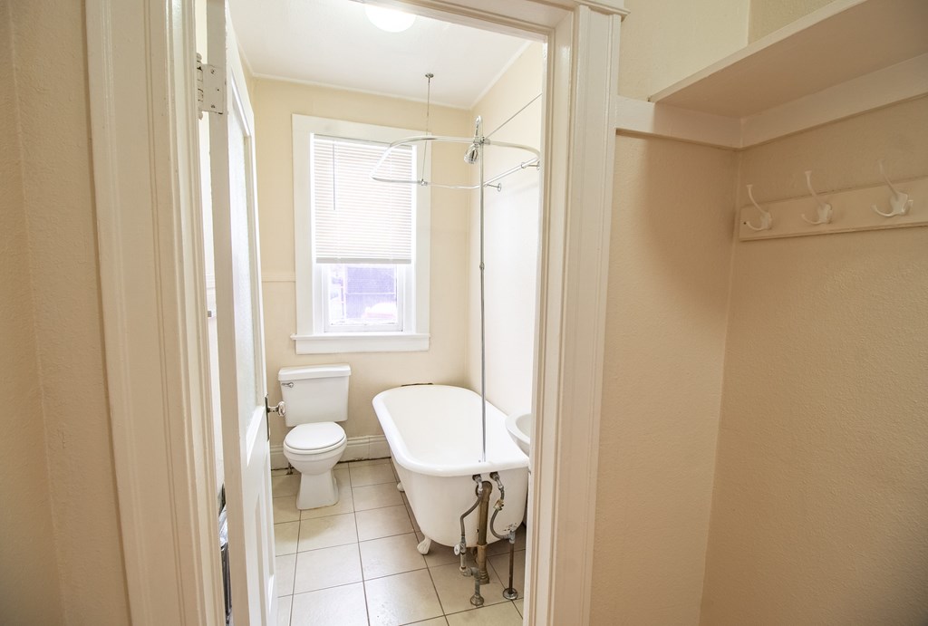 A white bathroom with a toilet, tub, and window.