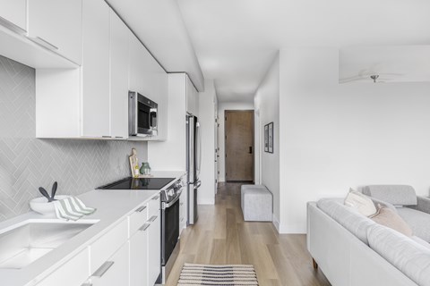 A modern kitchen with white cabinets and a grey sofa in the living room.