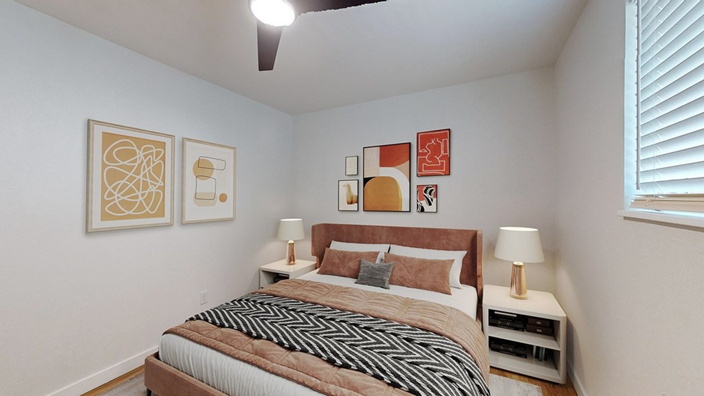 A bedroom with a bed, two lamps, and artwork on the wall.