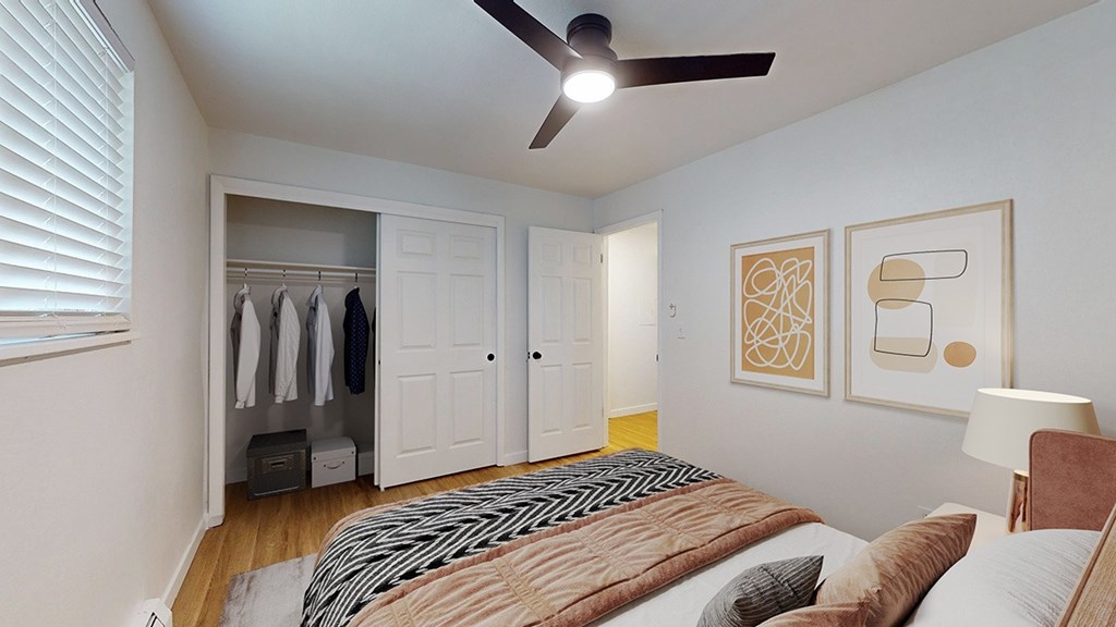 A bedroom with a bed, a ceiling fan, and a closet with clothes hanging.