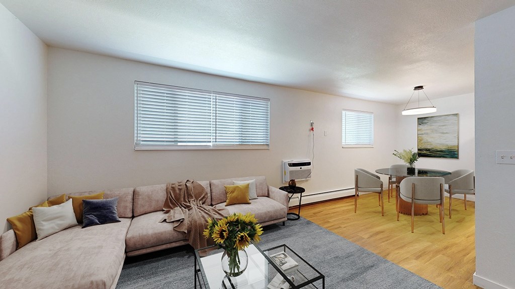 A living room with a grey couch, a glass coffee table, and a dining table with chairs.