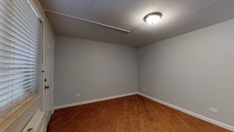 A room with wooden floors and a window with blinds.