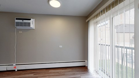 A room with a window covered by white blinds and a wall-mounted air conditioner.