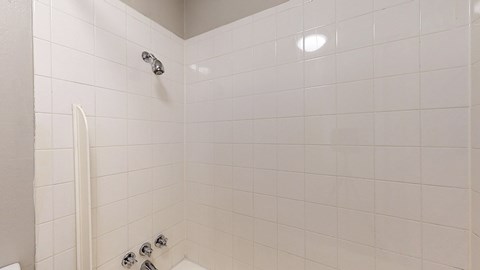 A white tiled shower with a white shower head and a white shower hose.