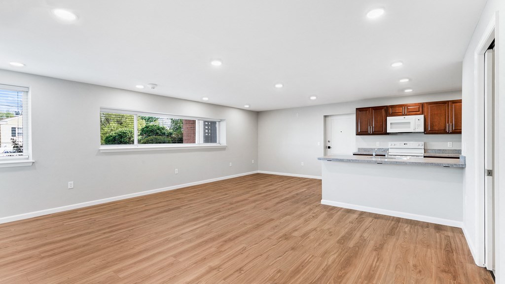 an empty living room with a kitchen and a window