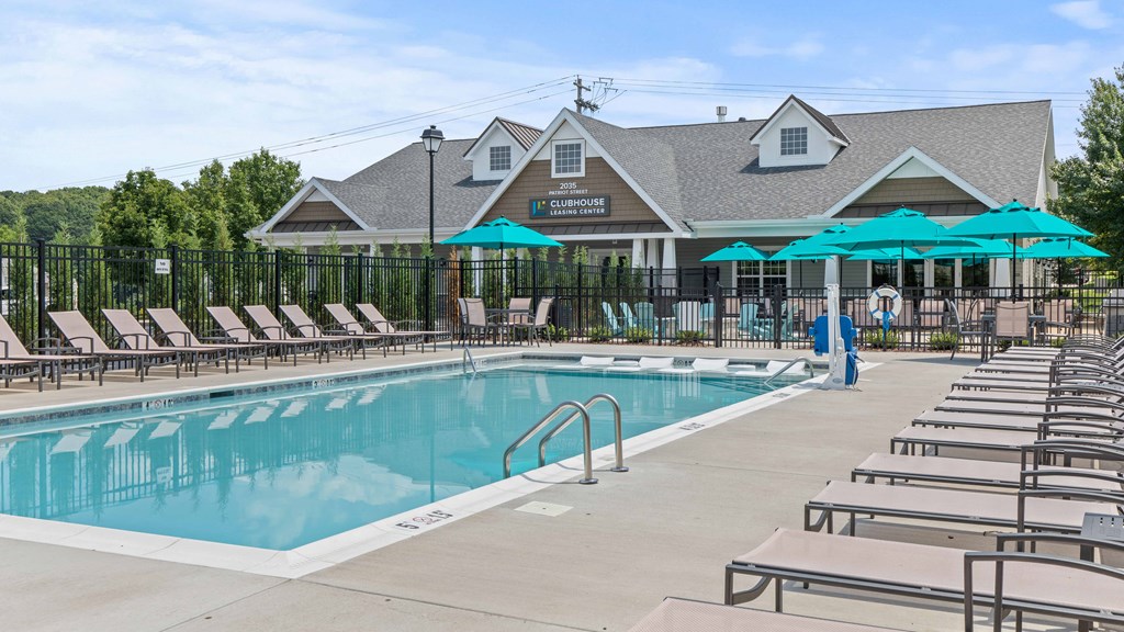 a swimming pool with chairs and umbrellas in front of a house