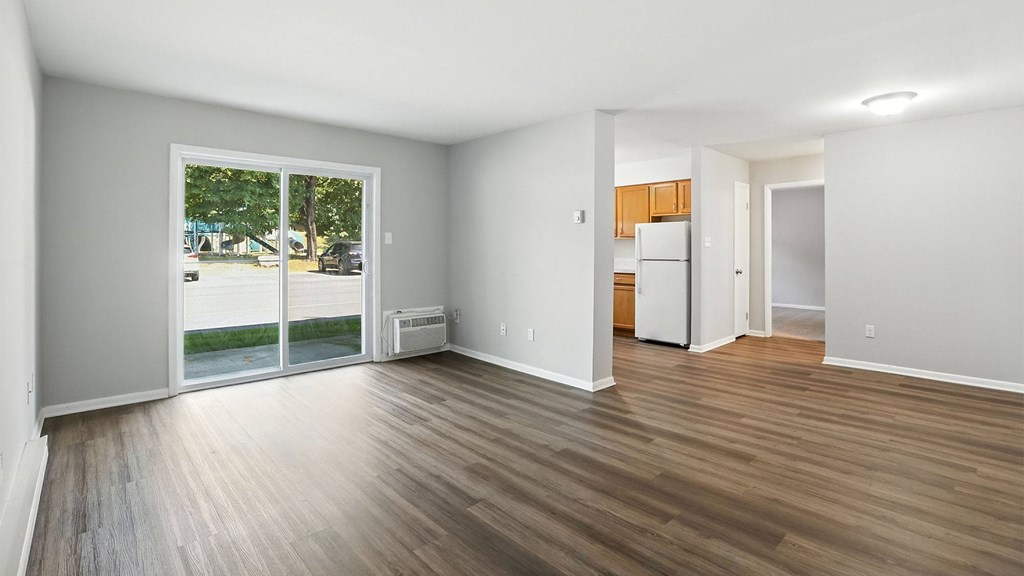 A room with wooden floors and white walls, with a view of a street through the sliding glass door.