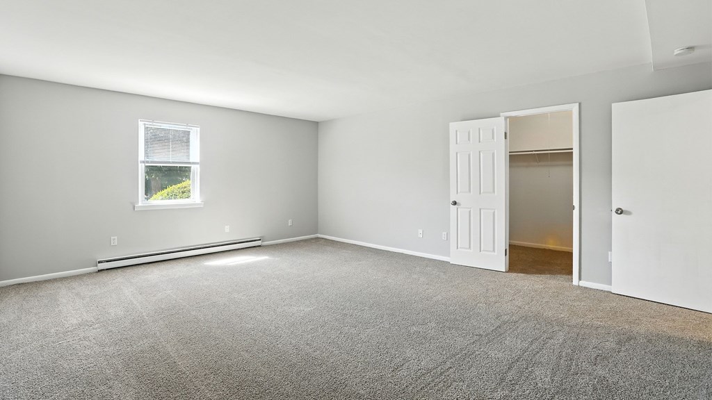 A room with a carpeted floor, a window, and a door.