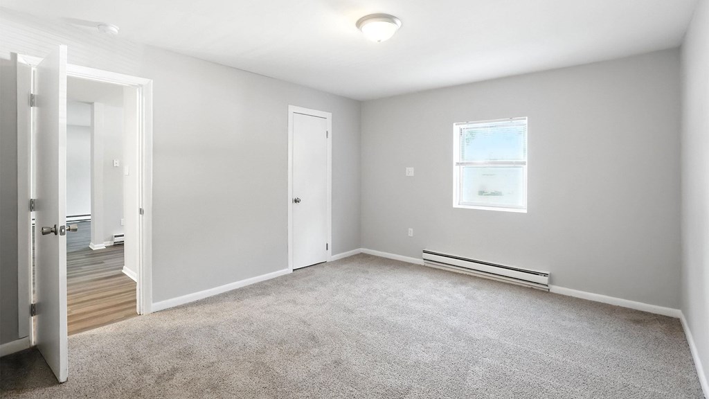 A room with a carpeted floor and a window with blinds.