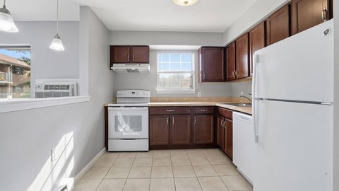 A white refrigerator is in the corner of a kitchen with brown cabinets.