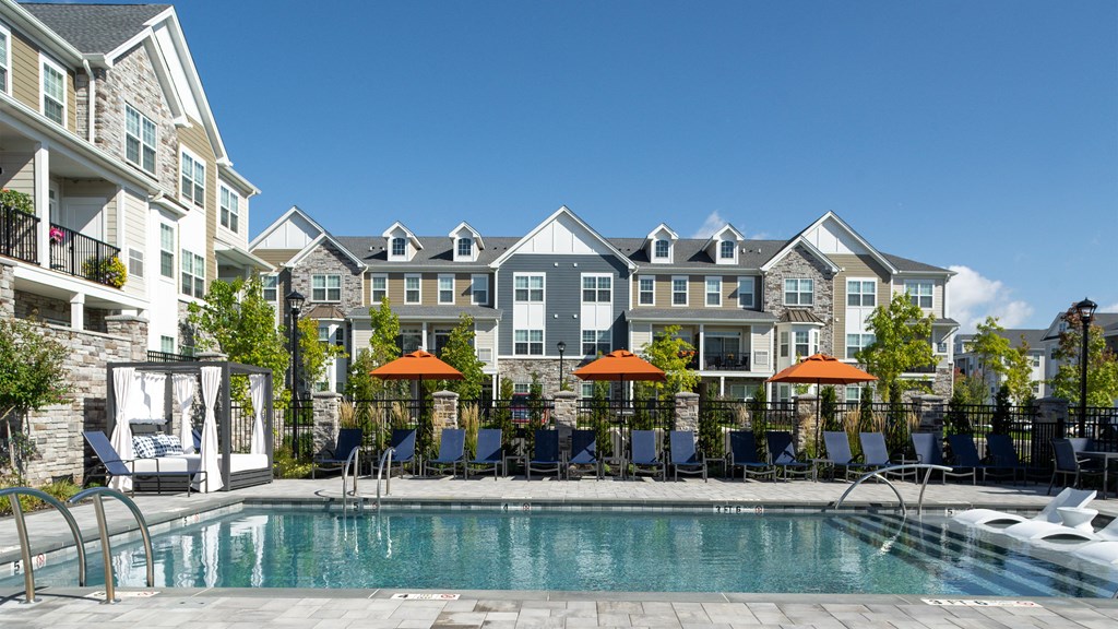 a swimming pool with chairs and umbrellas in front of an apartment building