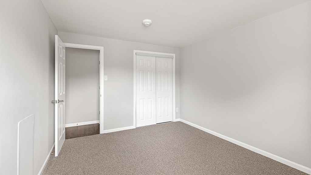 a bedroom with white walls and carpet and two doors