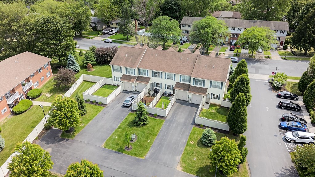 A large white building with a brown roof is surrounded by a grassy area and trees.