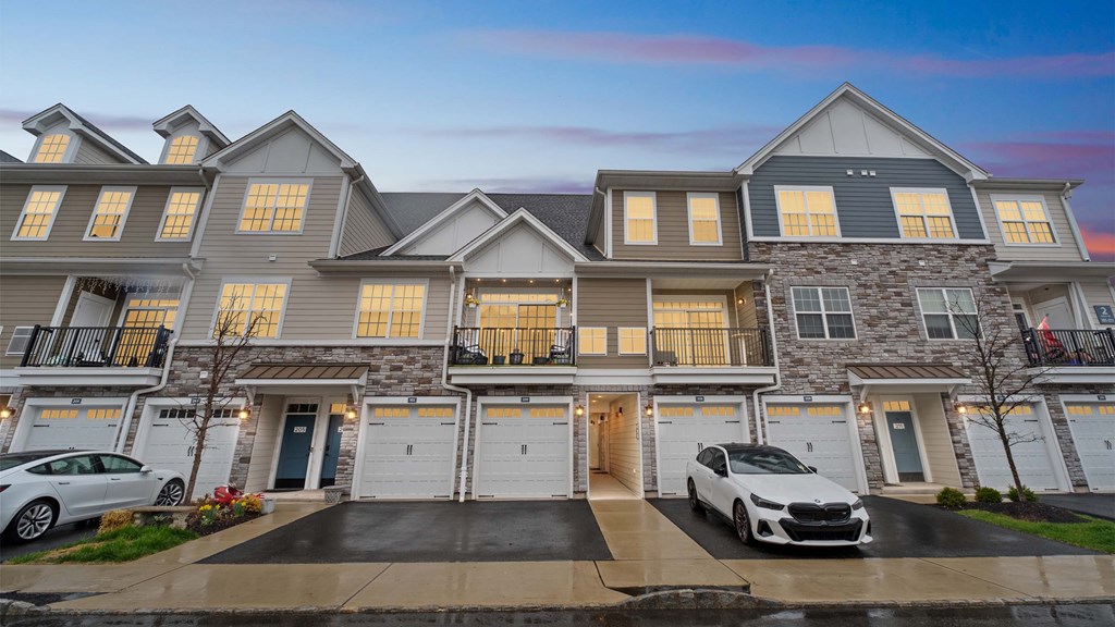 A large, modern house with a grey and white exterior and two cars parked in the driveway.