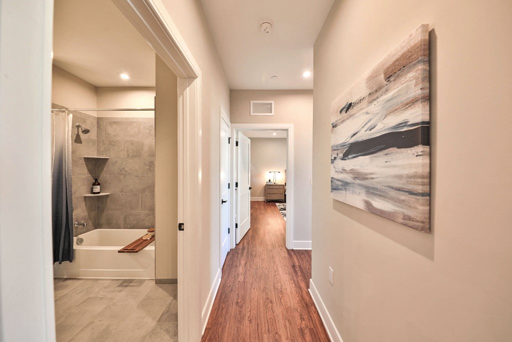 a hallway leading to a bathroom with a shower and a painting