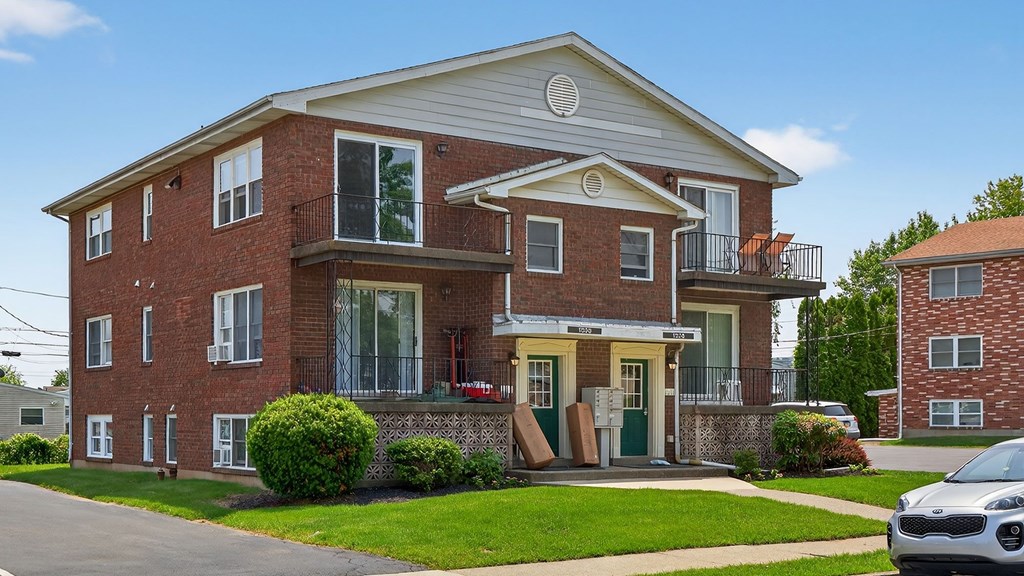 A red brick house with a white roof and a balcony on the second floor.