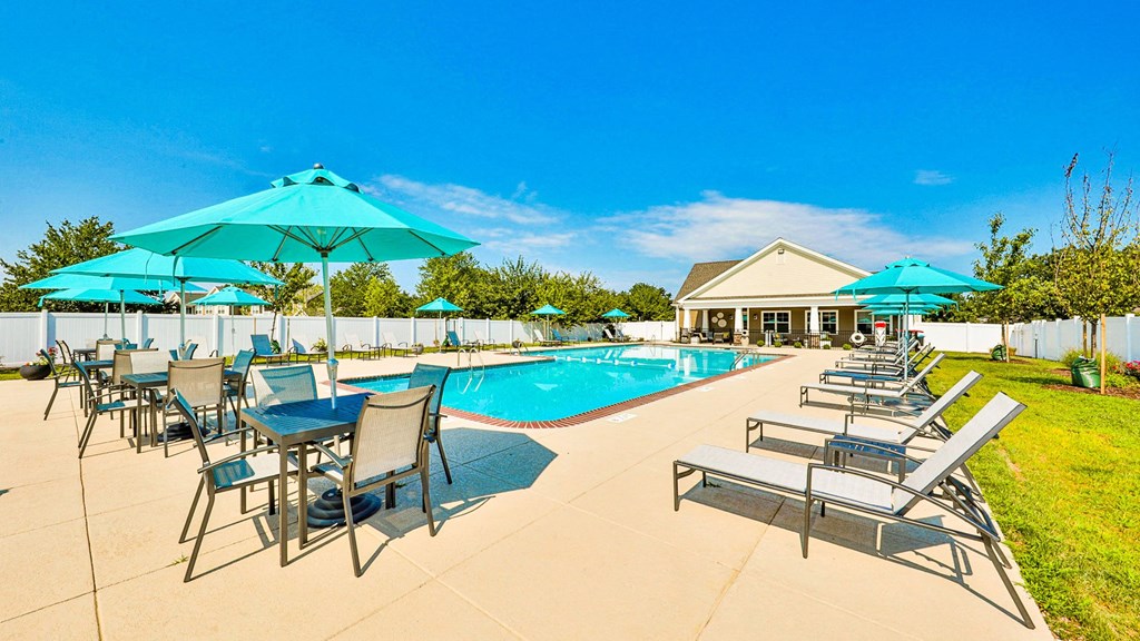 our resort style swimming pool is surrounded by chairs and umbrellas