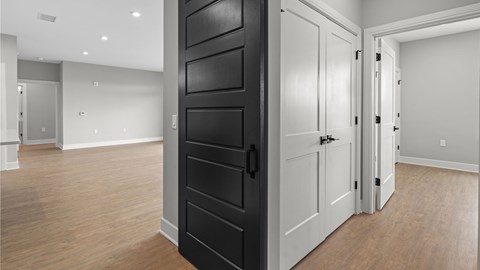A black door is in the middle of a room with white walls and wooden floors.