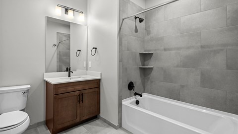 A bathroom with a white tub, sink, and grey tiled walls.