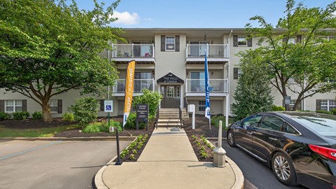 A black car is parked on the street in front of a building with a yellow banner.