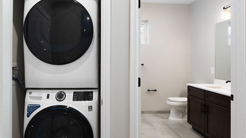 A white washing machine is in a bathroom with a toilet and sink.
