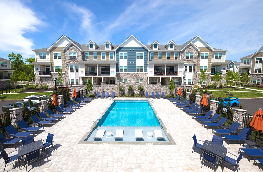 an outdoor pool with blue chairs and an apartment building in the background