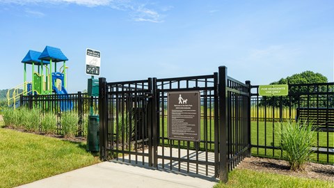 A black gate with a sign on it in front of a playground.