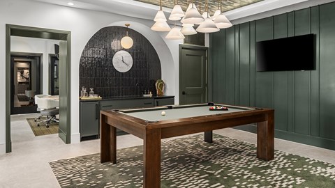 A pool table is in the middle of a room with a clock on the wall.