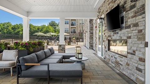 A patio with a grey couch and a stone fireplace.