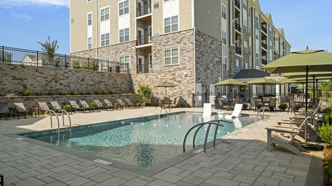 A swimming pool surrounded by a stone wall and lounge chairs.