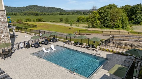 A large outdoor swimming pool surrounded by a black fence and lounge chairs.