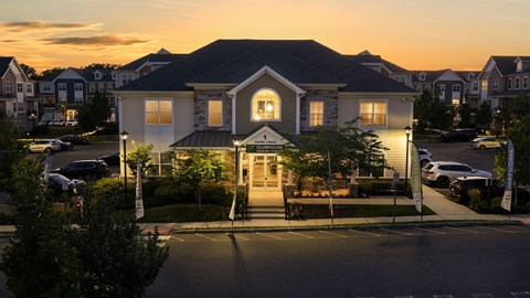 A building with a lit entrance and a parking lot in front.