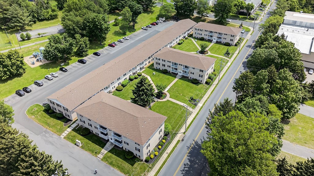 A large white building with a brown roof is surrounded by a grassy area and trees.