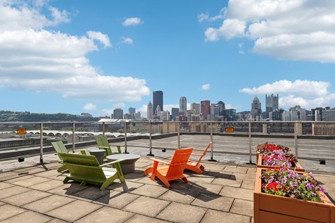 A rooftop patio with a table, chairs, and flowers with a city skyline in the background.