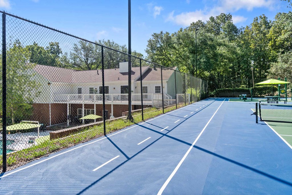 a tennis court with a fence and a house in the background