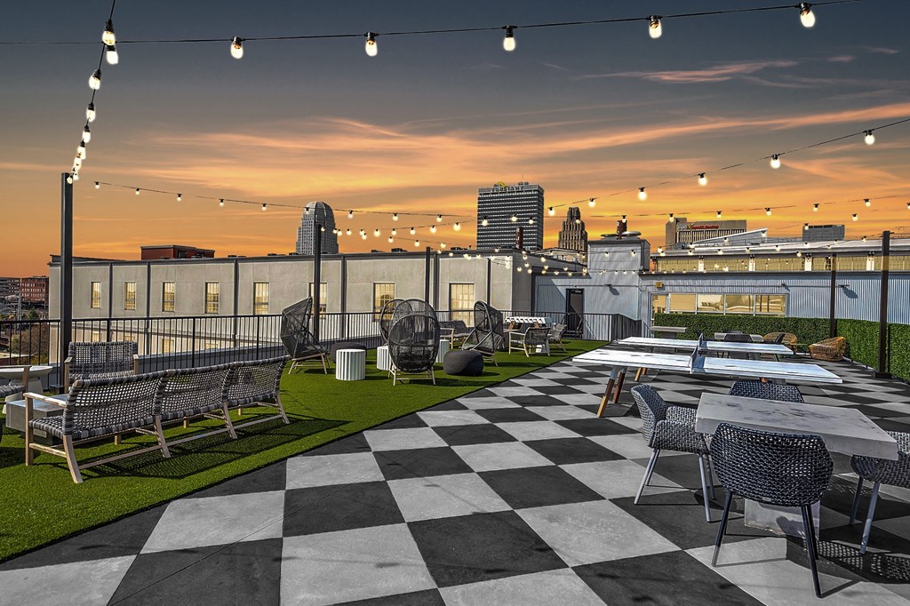 a rooftop patio with tables and chairs and a city skyline at sunset