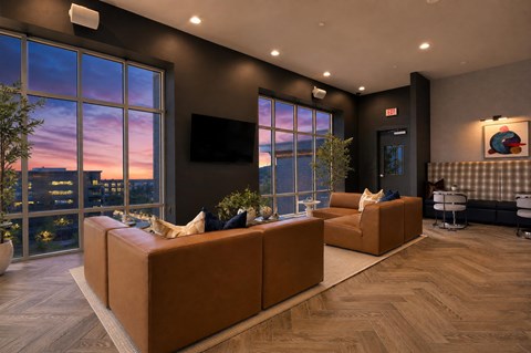 A modern living room with a large window overlooking the city at dusk.