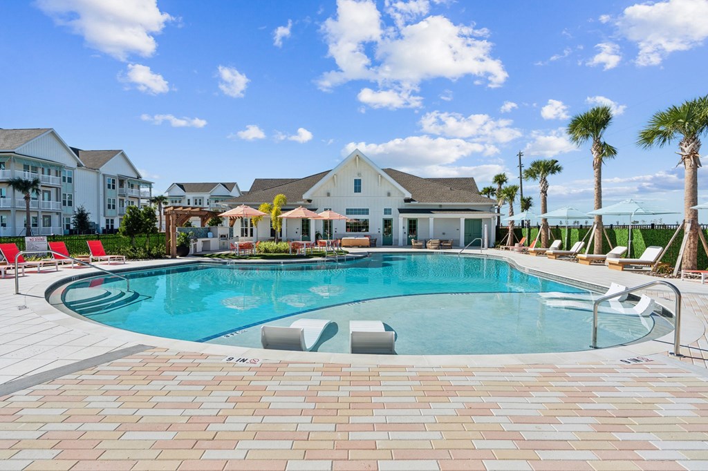A large swimming pool surrounded by a brick patio and lounge chairs.