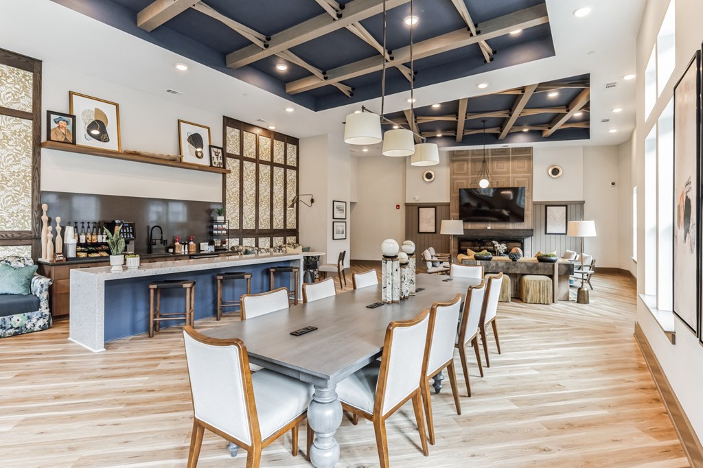 a long dining table with chairs in a room with a kitchen and a living room
