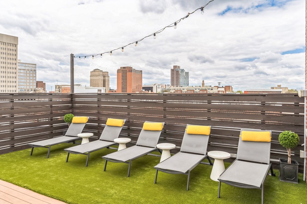 a row of lounge chairs on a rooftop patio with a view of the city