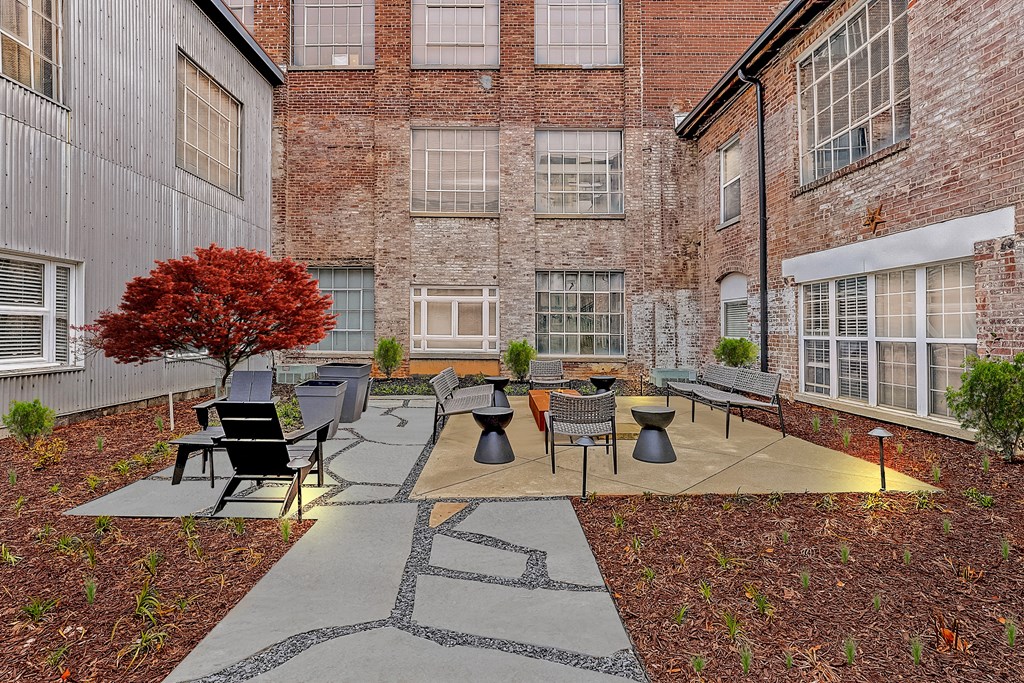 a courtyard with a tree and several chairs and tables in front of a brick building