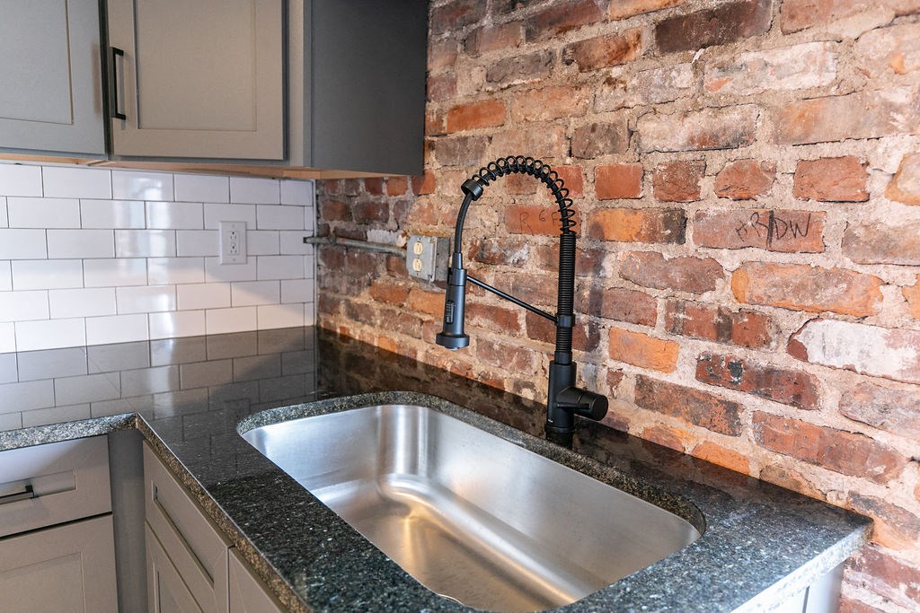 a kitchen sink next to an exposed brick wall