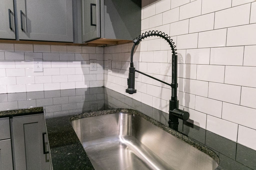 a stainless steel sink in a white tiled kitchen with a black faucet