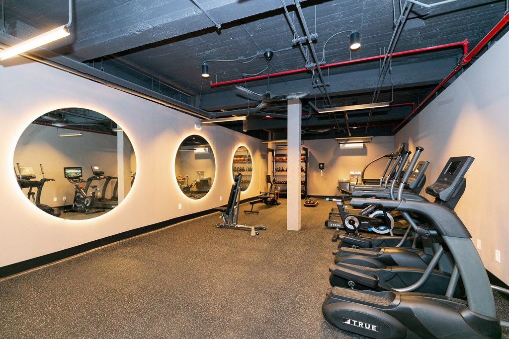 a gym with cardio machines and round mirrors on the wall